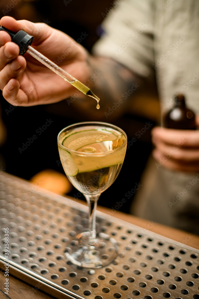 barman holds dropper with liquid and adds it to glass with cocktail