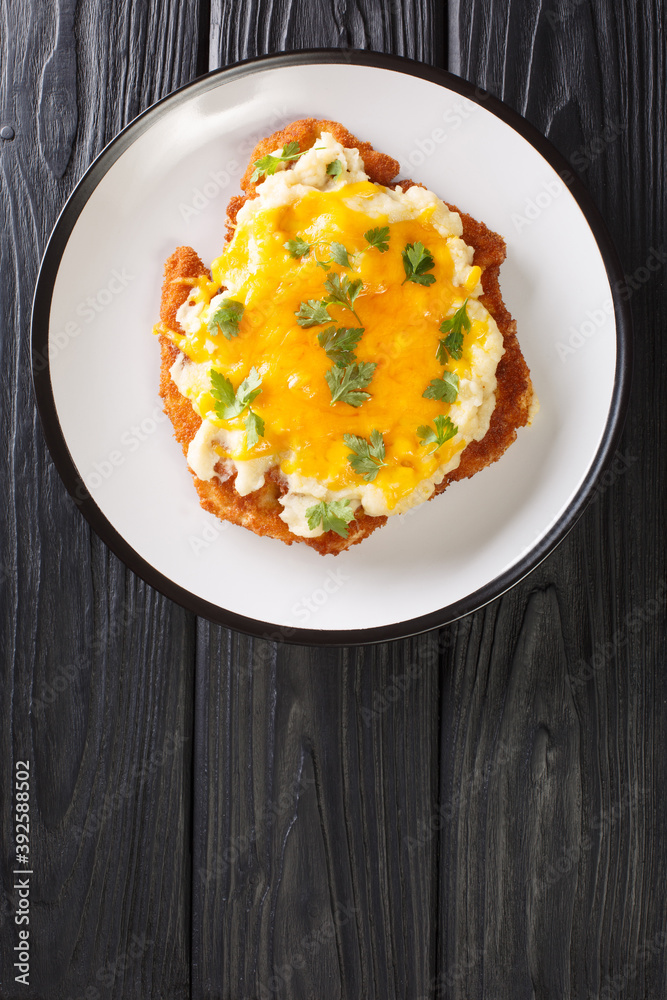 English fast food Parmo with chicken fillet breaded with bechamel sauce and cheddar cheese close-up in a plate on the table. vertical top view from above