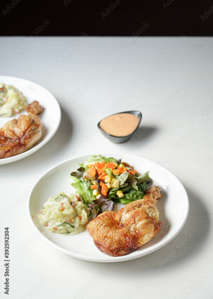 plate of delicious grilled chicken legs steak with vegetable and salad potato on white background plate of delicious grilled chicken legs steak with vegetable and salad potato on white background