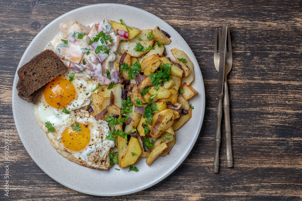 Ukrainian food, fried potatoes with onions, eggs, vegetable salad, black bread on wooden background Ukrainian food, fried potatoes with onions, eggs, vegetable salad, black bread on wooden background