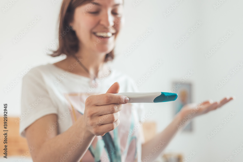 Happy woman sitting on the bed, checking pregnancy test. Result positive, “Schwanger” Happy woman sitting on the bed, checking pregnancy test. Result positive, “Schwanger”