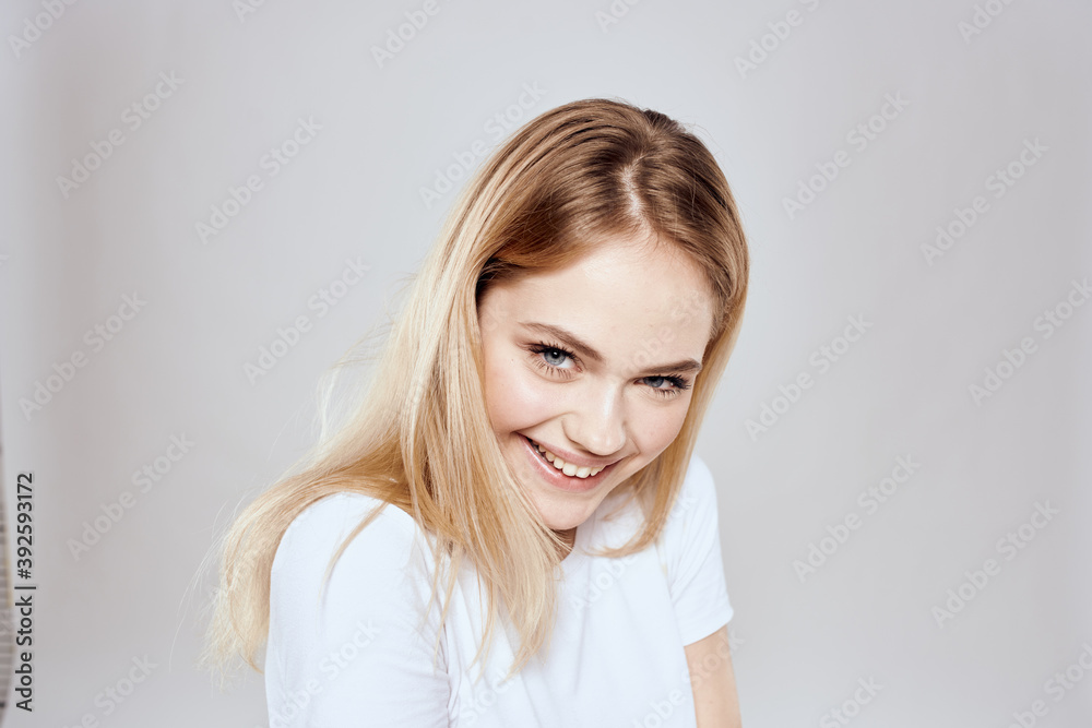 cheerful blonde in a white t-shirt gesturing with her hands light background cheerful blonde in a white t-shirt gesturing with her hands light background