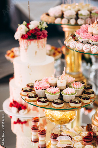 Festive candy bar with cake, macaroons, desserts and fruit decorated with flowers on a round table