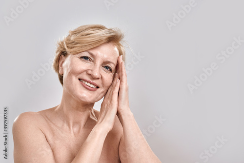 Close up portrait of beautiful middle aged woman in underwear looking at camera, showing sleep gesture while posing isolated against grey background