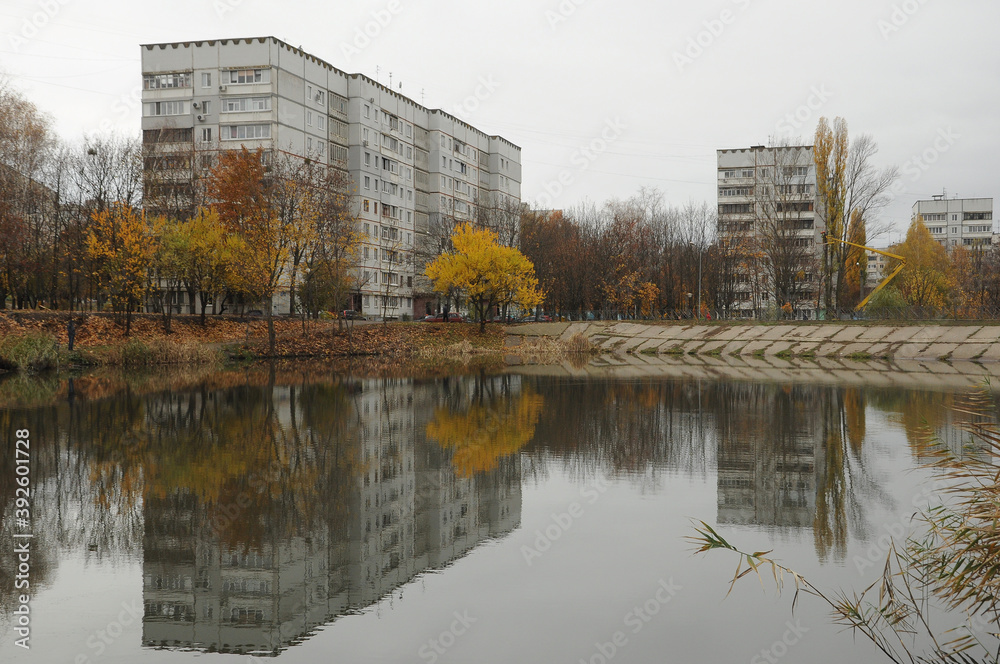 Autumn city landscape. Multi-storey buildings and trees with yellow leaves reflected in the water.