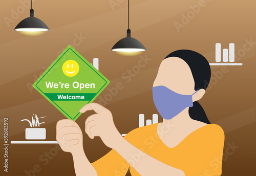 Business owner wearing protective face mask and hanging open sign at her restaurant