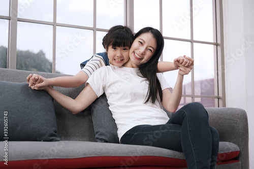 Smiling Asian girl child is hugging and playful with mother on sofa in living room. Family on holiday concept.