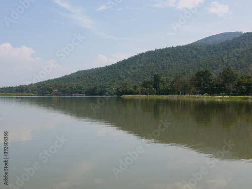 Green hill, blue sky, white clouds, and a reservoir with reflection in the water - relaxing landscape