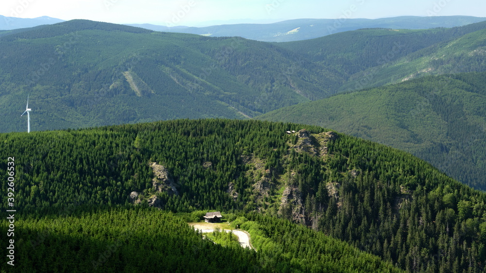 Obraz premium Enlightened small wooden hut in the middle of forested hills with prominent rock formations in the background.