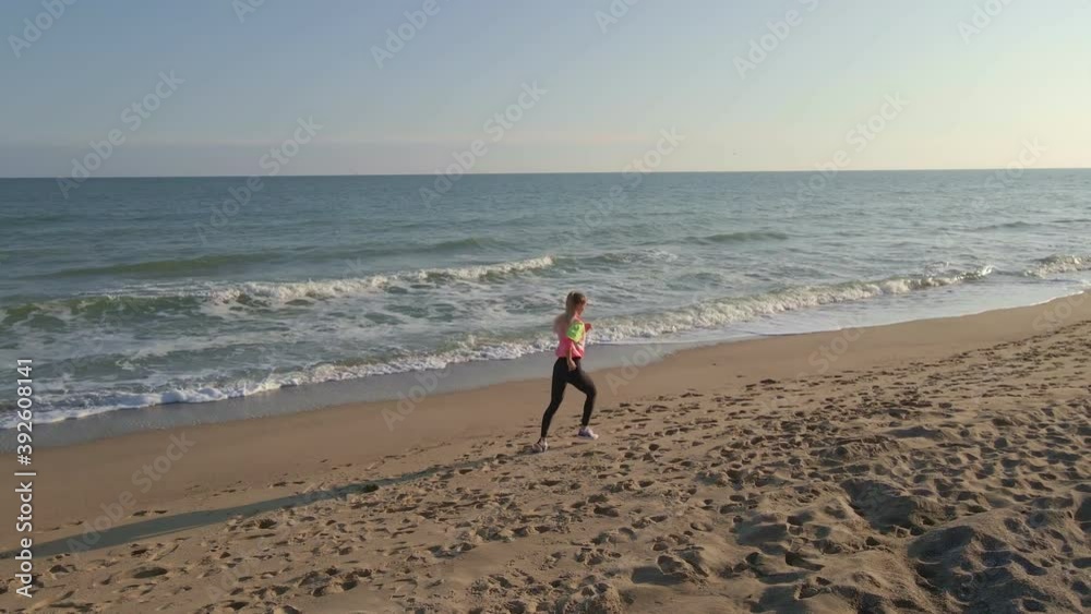 young fit woman jogging along the beach near the sea at sunset, sports, recreation, areal view of female jogger at the seaside young fit woman jogging along the beach near the sea at sunset, sports, recreation, areal view of female jogger at the seaside