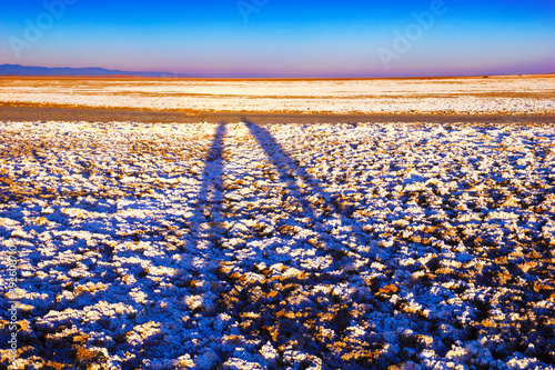 Beautiful nature view - dried white salt crust with two elongated people shadows on the surface of Namak lake at the background of blue sky at sunset time in Maranjab desert, Kashan, Iran, Middle East photo