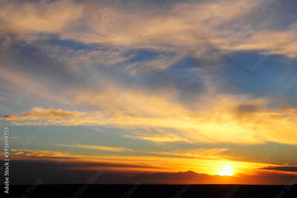 Beautiful dramatic sunset, setting sun, distant mountain range, black desert at the background of blue sky with feather clouds, evening in Maranjab desert, Aran va Bidgol, Iran, Middle East