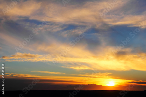Beautiful dramatic sunset  setting sun  distant mountain range  black desert at the background of blue sky with feather clouds  evening in Maranjab desert  Aran va Bidgol  Iran  Middle East