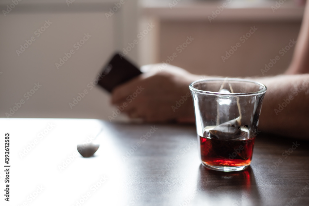There is a glass of unfinished tea on the table. A man with a phone is nearby, a blurred background. Loneliness and problems