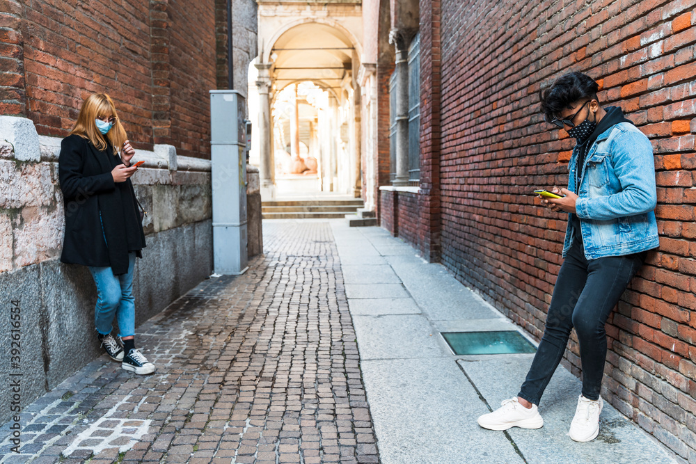 young multiethnic couple with protective masks using smartphones