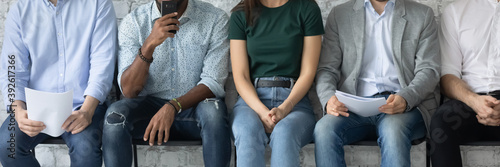 Wide cropped image of five diverse millennial people unemployed specialists applicants candidates on place in corporate workforce sitting in row expecting for invitation on interview. Panoramic banner