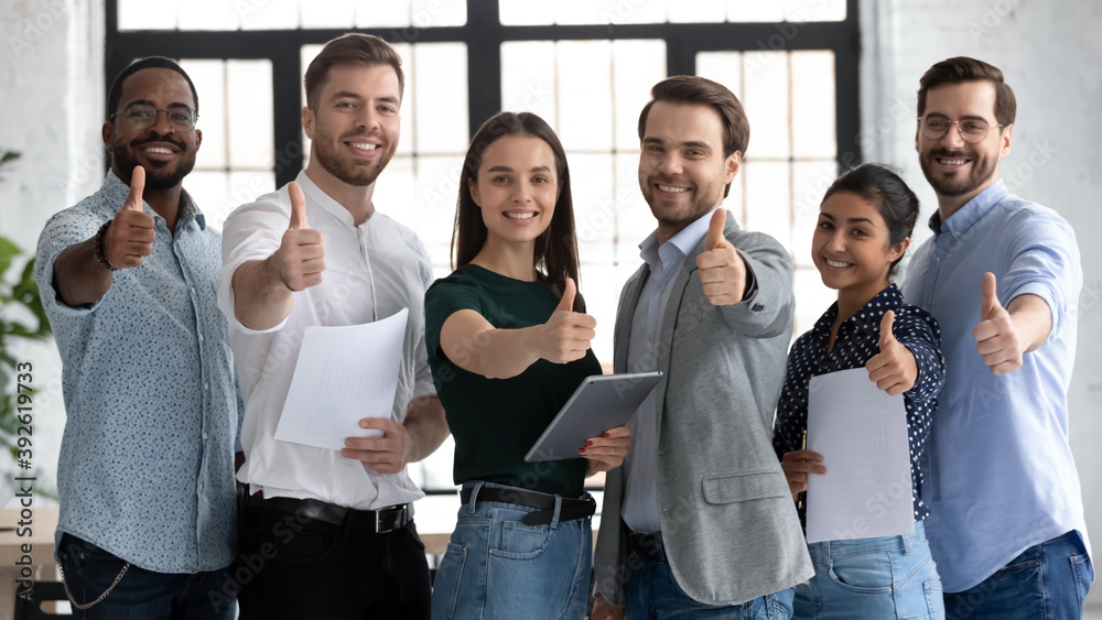 © fizkes - We are glad to recommend. Young modern team of diverse qualified specialists posing for portrait in corporate office looking at camera showing thumb up gesture approving product service able to help © fizkes - We are glad to recommend. Young modern team of diverse qualified specialists posing for portrait in corporate office looking at camera showing thumb up gesture approving product service able to help