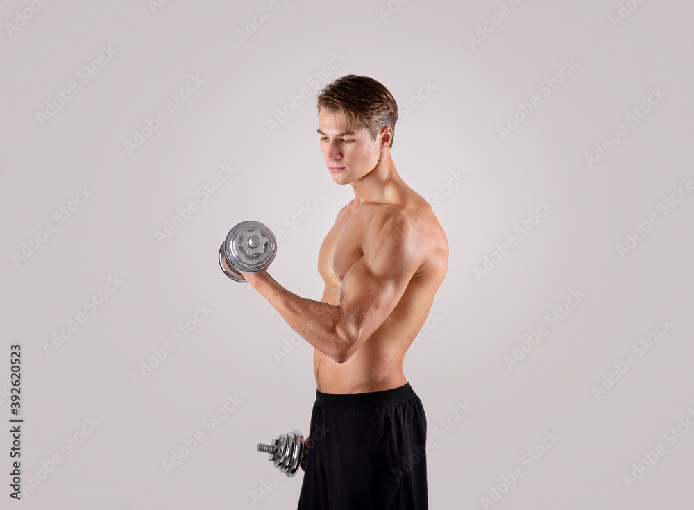 Handsome Caucasian bodybuilder pumping up iron, exercising with dumbbells over light studio background Handsome Caucasian bodybuilder pumping up iron, exercising with dumbbells over light studio background