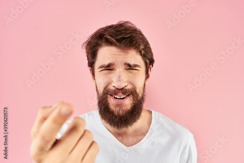 Bearded man in white t-shirt gesturing with hands facial expression close up pink background