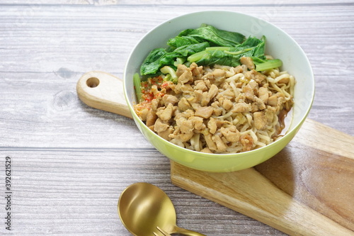 Mie Ayam or Indonesian chicken noodles topped with sweet sauce chicken, mustard greens and chili sauce on wooden background as a local street food photo