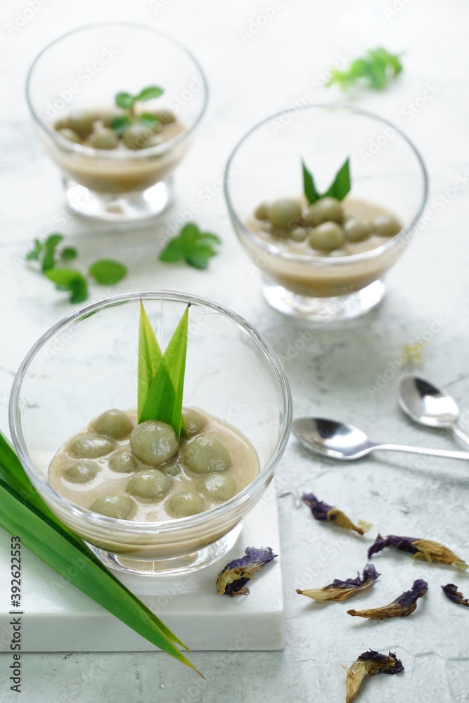 Shiny background for Kolak Putri Mandi or glutinous rice ball compote with pandan leaves, dried butterfly pea flowers and some mints. Selective focus