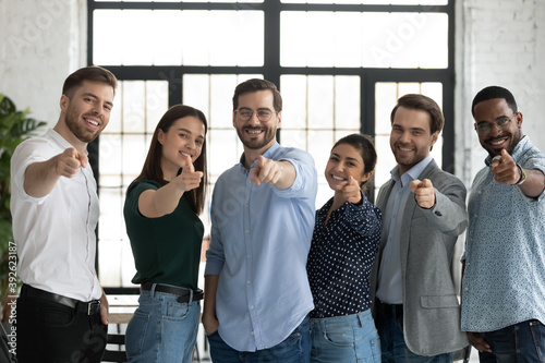 We are waiting for you. Group portrait of friendly successful diverse staff multiethnic teammates young men and women standing in row at office pointing fingers at camera choosing new colleague client