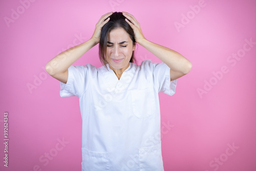 Fotografie Young brunette doctor girl wearing nurse or surgeon uniform over isolated pink b
