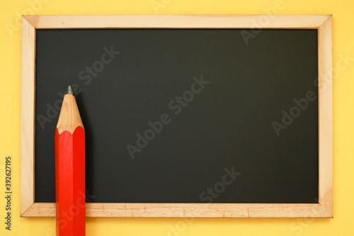 A black chalkboard with a red pencil isolated on the yellow background 