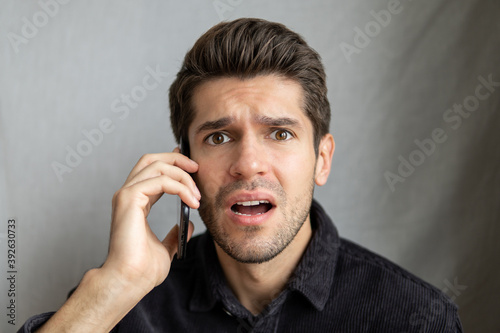 Portrait of a young beautiful man talking on the mobile phone with a shocked face expression in a shirt 