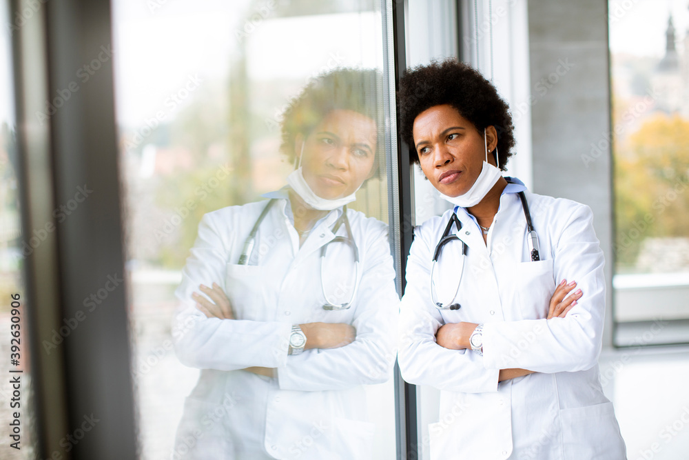 Black female doctor standing by the office window with negative expression Black female doctor standing by the office window with negative expression