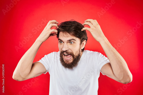 Emotional bearded man gestures with his hands in a white T-shirt aggression discontent red background