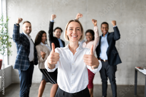 Businesswoman Gesturing Thumbs-Up Standing With Joyful Employees Team In Office photo