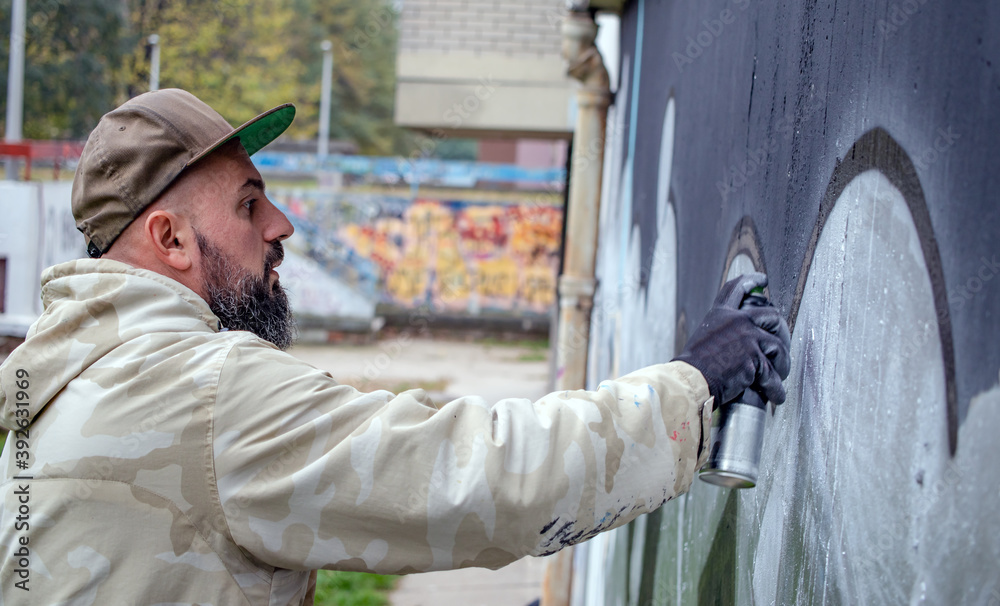 Street graffiti artist in action, drawing with spray paint can on the ...