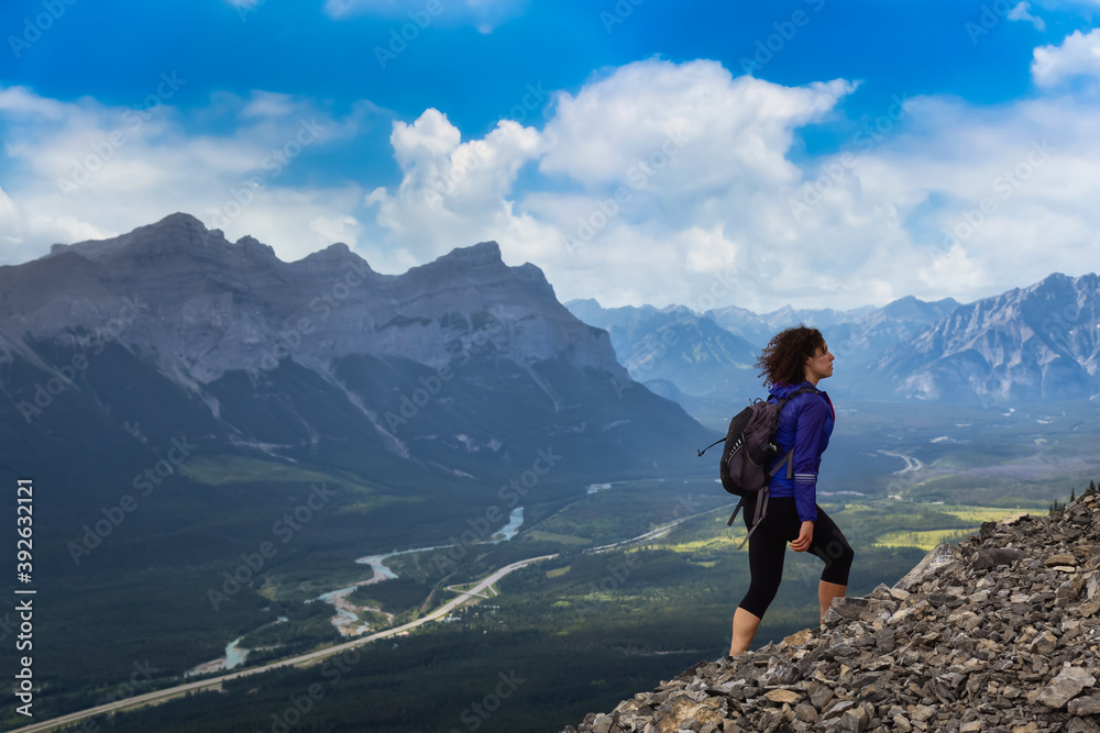 Adventurous Girl is hiking up a rocky mountain. Cloudy Sunny Sky. Taken from Mt Lady MacDonald, Canmore, Alberta, Canada.