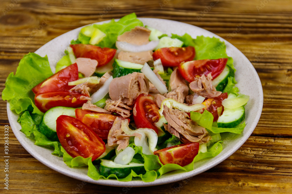 Tasty tuna salad with lettuce and fresh vegetables on wooden table