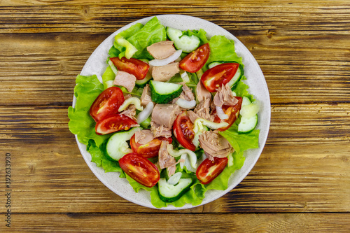 Tasty tuna salad with lettuce and fresh vegetables on wooden table. Top view