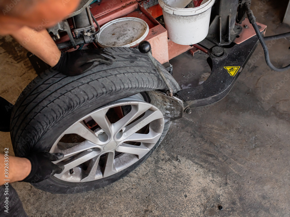 Mechanic with pneumatic wrench unscrews the wheel. Male professional mechanic at a car garage fixing a wheel. Mechanic repairing a car wheel. Mechanic with pneumatic wrench unscrews the wheel. Male professional mechanic at a car garage fixing a wheel. Mechanic repairing a car wheel.