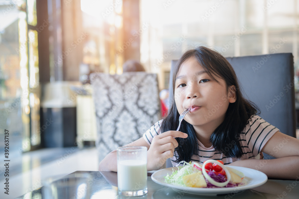 Asian cute little girl eating fresh tomato and salad on morning.