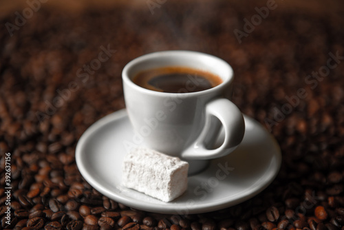 Cup of fresh hot coffee with Turkish delight on a saucer and coffee beans.