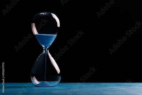 Sandglass, egg timer with blue sand on black background, time passing concept for business deadline