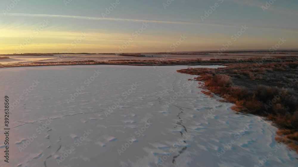 custom made wallpaper toronto digitalDrone flying just above a frozen lake that is covered by snow drifts at sunset. Frost covered trees line the lakeshore and the sky is highlighted with yellow clouds.