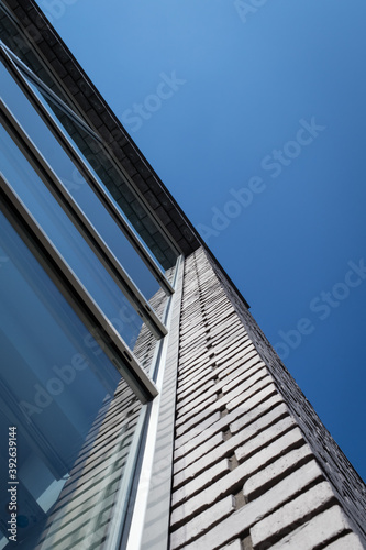 Abstract viewpoint of an exterior facade of a modern office, partly glass and partly brickwork set against a blue sky.