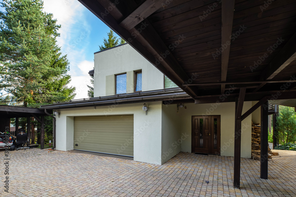 Modern exterior of luxury private house with built-in closed garage. Wooden canopy. Close door. Woodpile near wall. Modern exterior of luxury private house with built-in closed garage. Wooden canopy. Close door. Woodpile near wall.