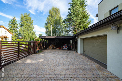Modern exterior of luxury private house with built-in closed garage. Toys and woodpile under wooden canopy. Sunny summer day.