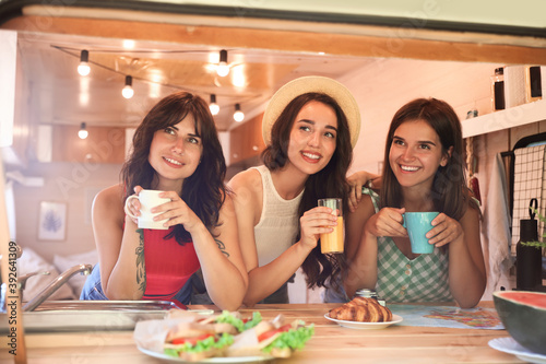 Happy young women having breakfast in trailer. Camping vacation