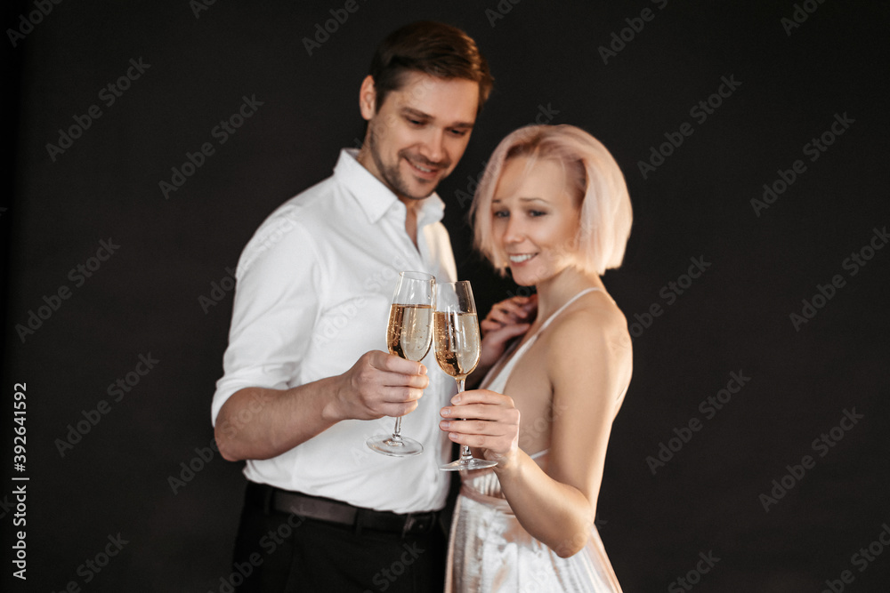 Beautiful happy couple young family in evening dresses with glasses of champagne on dark background Beautiful happy couple young family in evening dresses with glasses of champagne on dark background