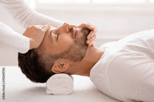 Sleeping man getting healing face massage at spa