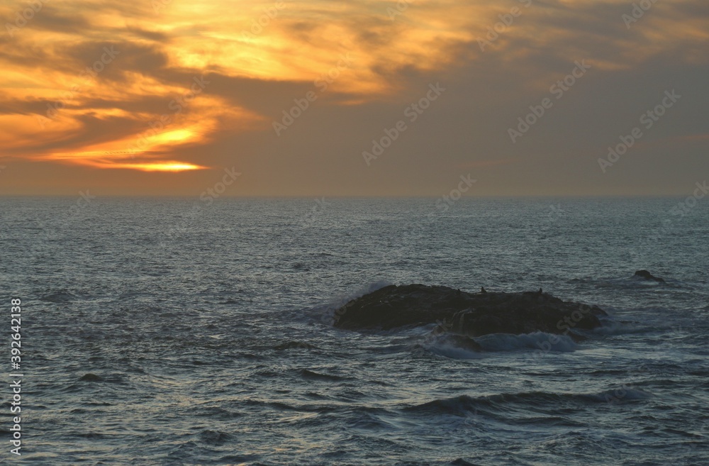 Sunset on the shore of the wild atlantic ocean at high tide. Rocks and waves. Barely recognizable seals on a rock. Yzerfontein, South Africa. 