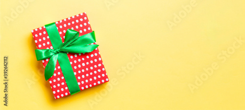 wrapped Christmas or other holiday handmade present in paper with green ribbon on yellow background. Present box, decoration of gift on colored table, top view with copy space