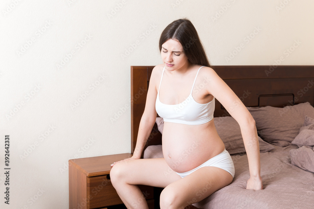 beautiful pregnant woman touching her tummy and keeping one hand on her back at home on bed beautiful pregnant woman touching her tummy and keeping one hand on her back at home on bed